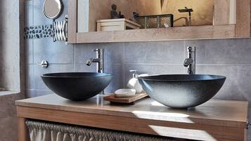 A bathroom with a wooden vanity, two vessel sinks, a mirror, and a light fixture above the mirror.