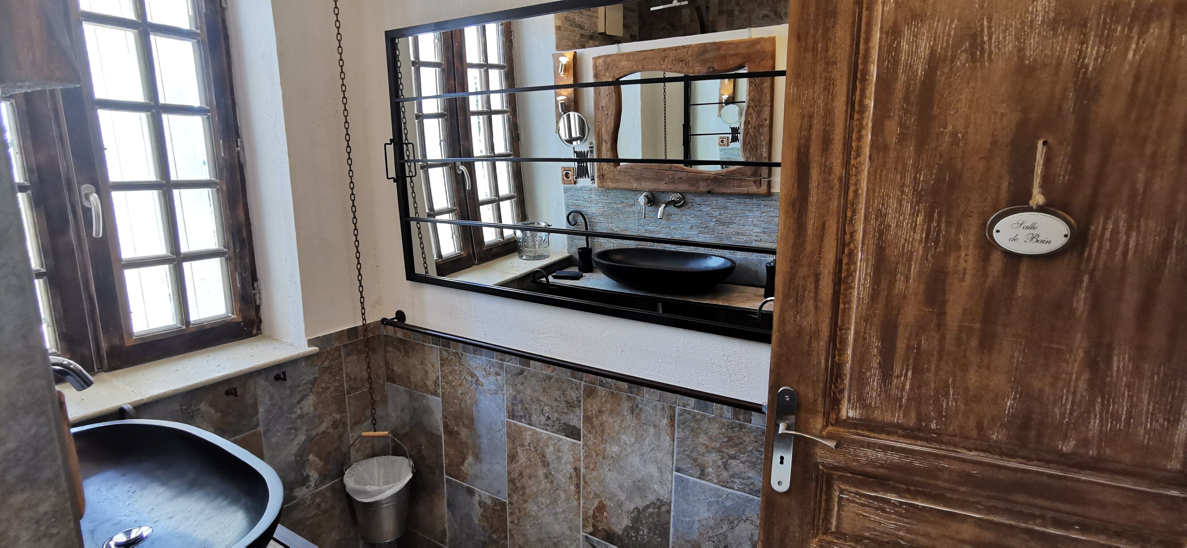 A bathroom with a large mirror, a black sink, and a wooden door.