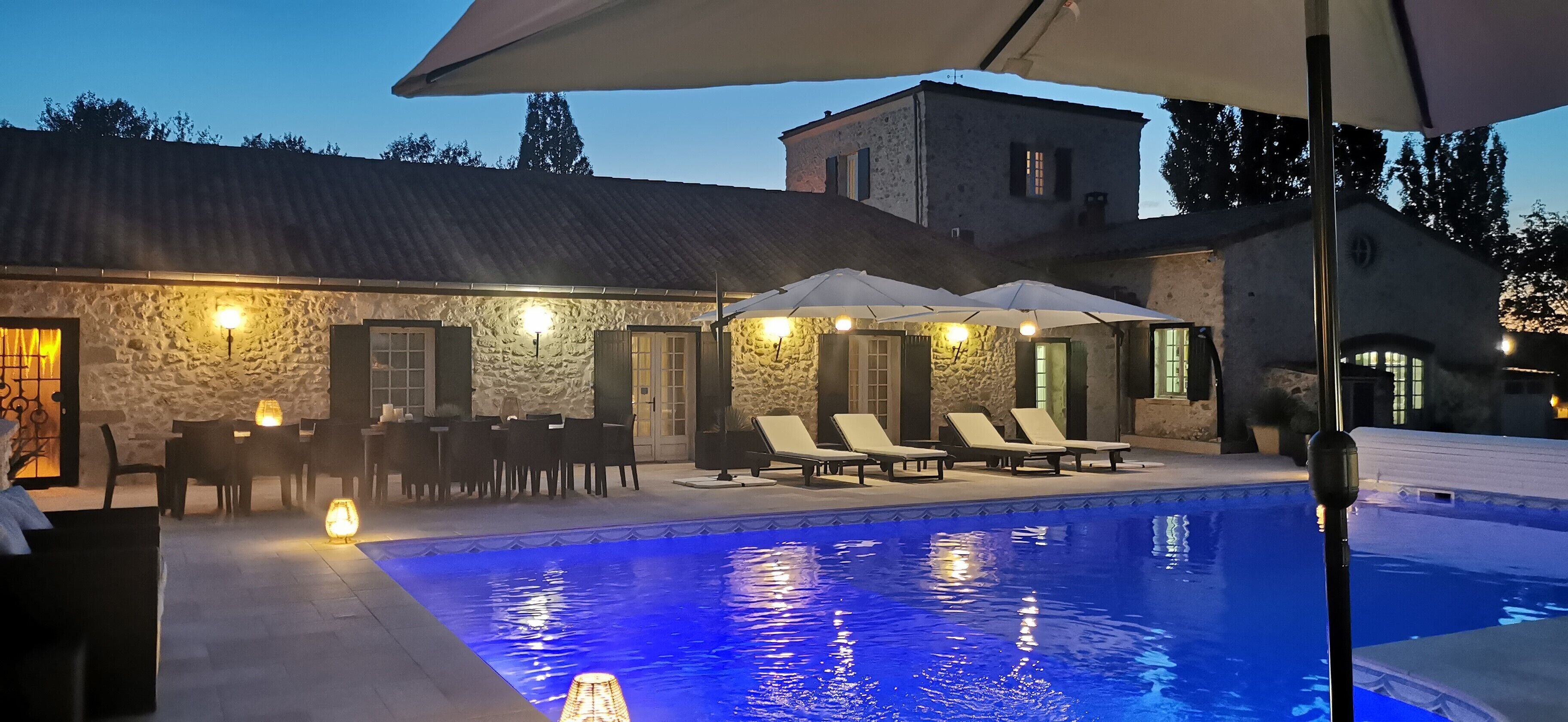 A stone building with a swimming pool, outdoor seating, and umbrellas.