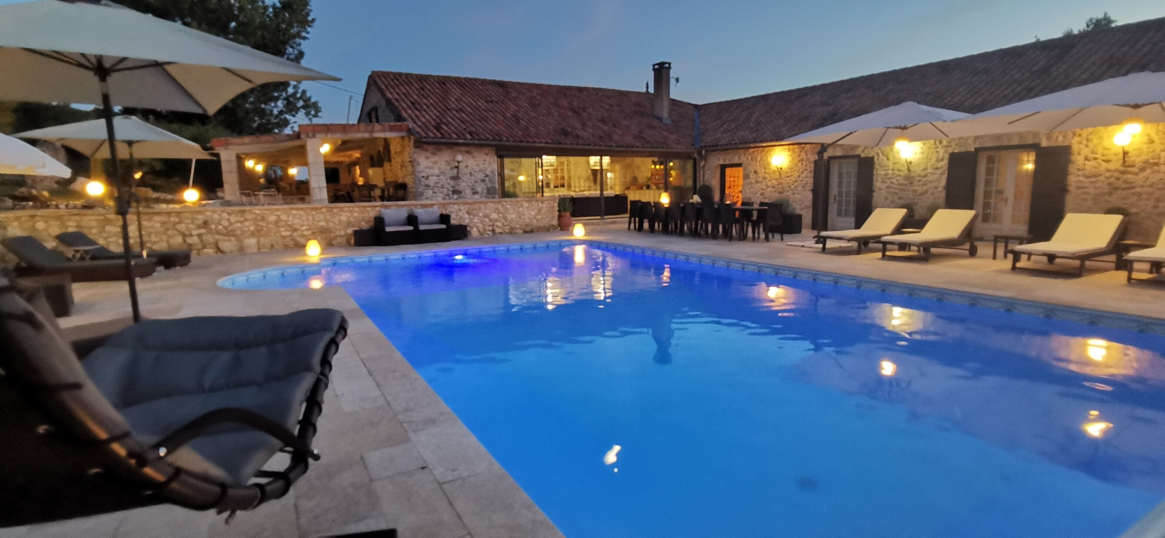 Una piscina con sillas de descanso y sombrillas, paredes de piedra y un edificio de piedra con techo de tejas.
