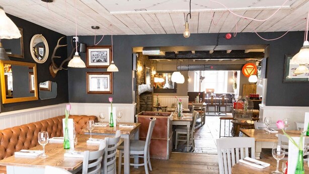Un restaurant avec des tables et des chaises en bois, un coin bar et des tableaux encadrés aux murs.