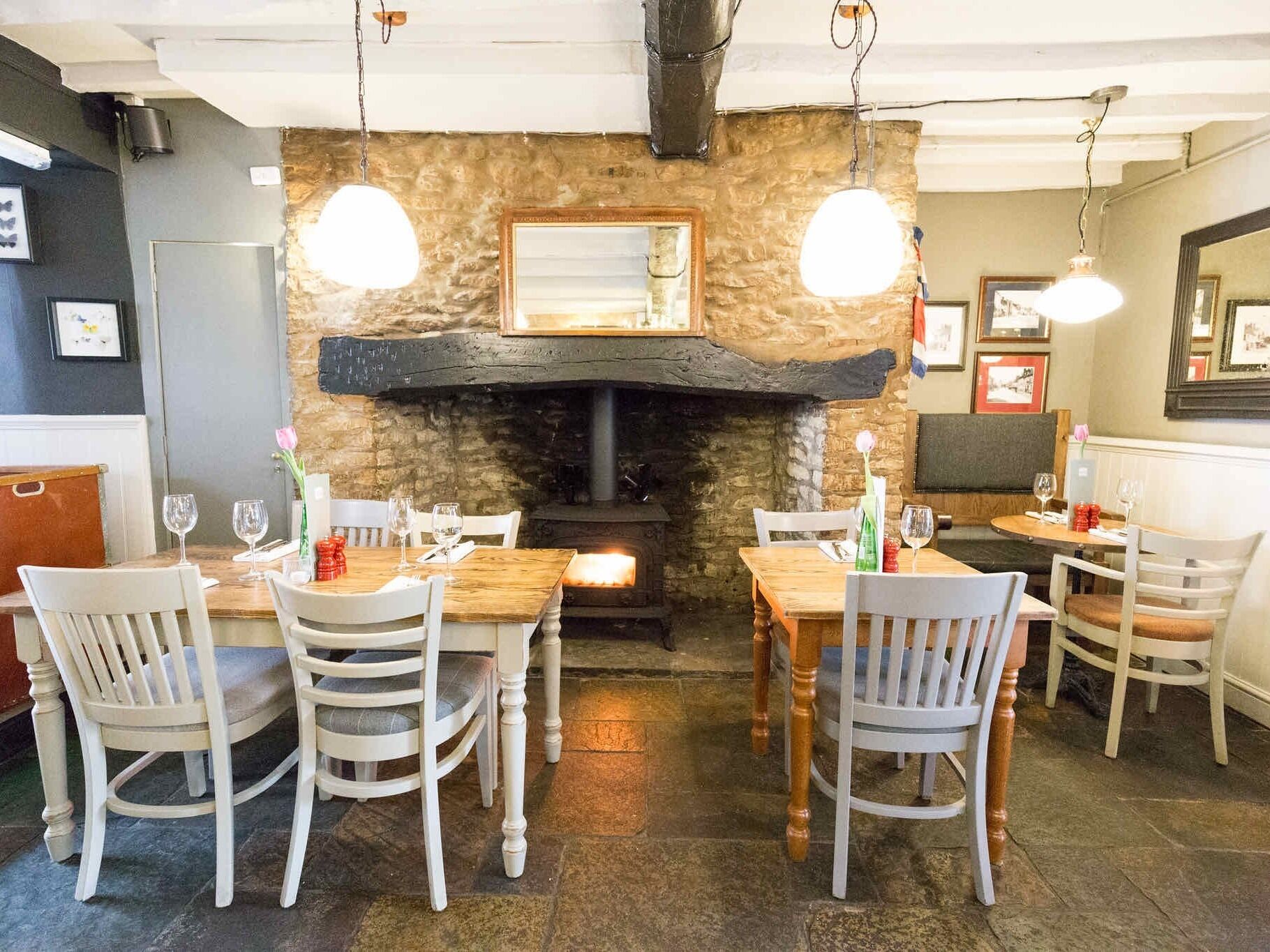 Un restaurante con chimenea de piedra, mesas de madera y sillas blancas.