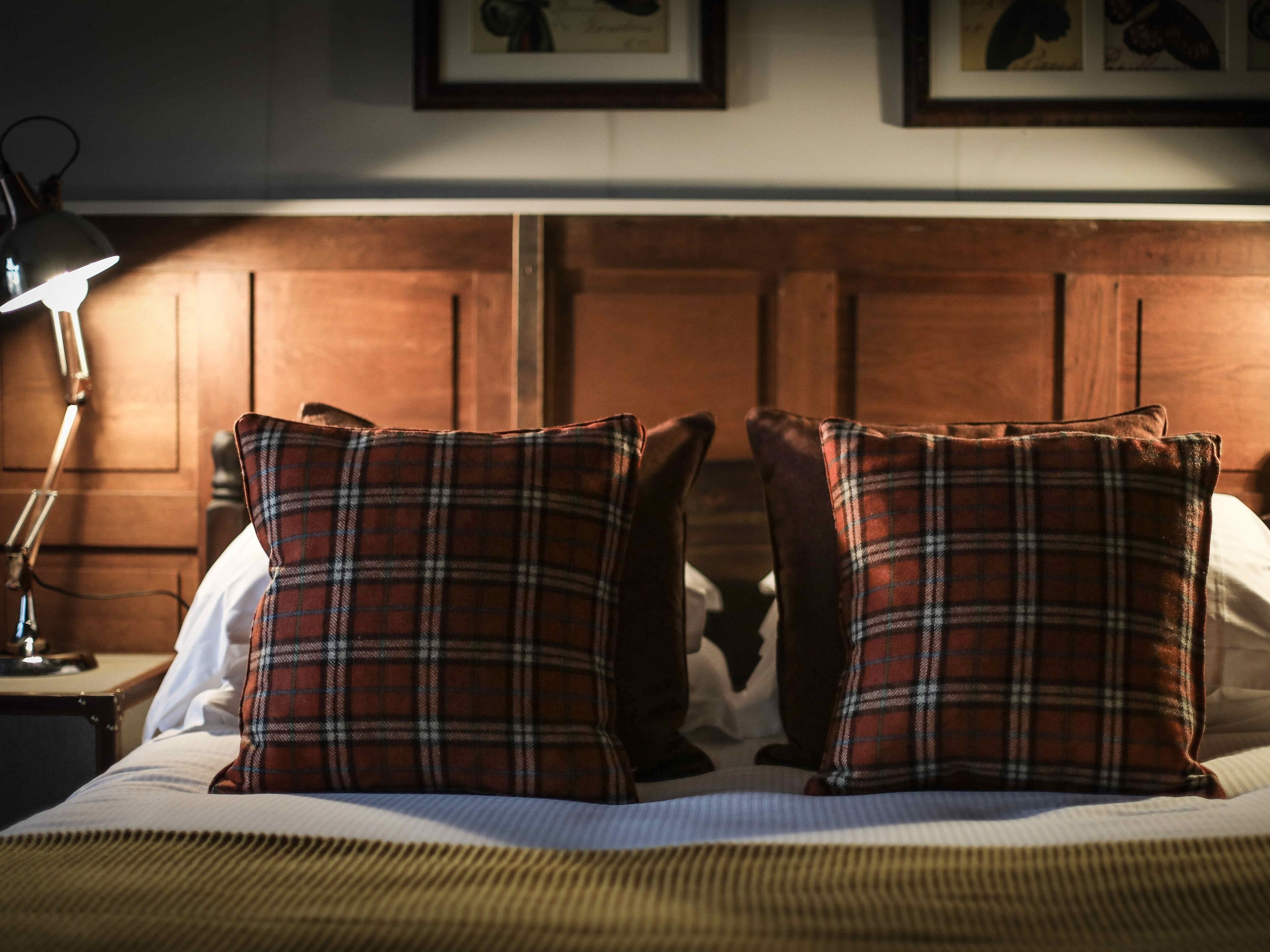 A bed with plaid pillows, a wooden headboard, and a bedside lamp.