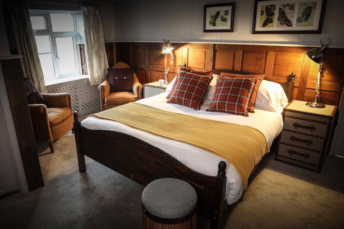 A cozy bedroom with a wooden bed, two bedside lamps, a chair, a nightstand, and a window with curtains.