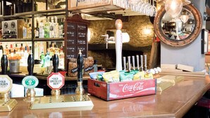 Un espace bar avec différentes bouteilles, des verres et une boîte de Coca-Cola.