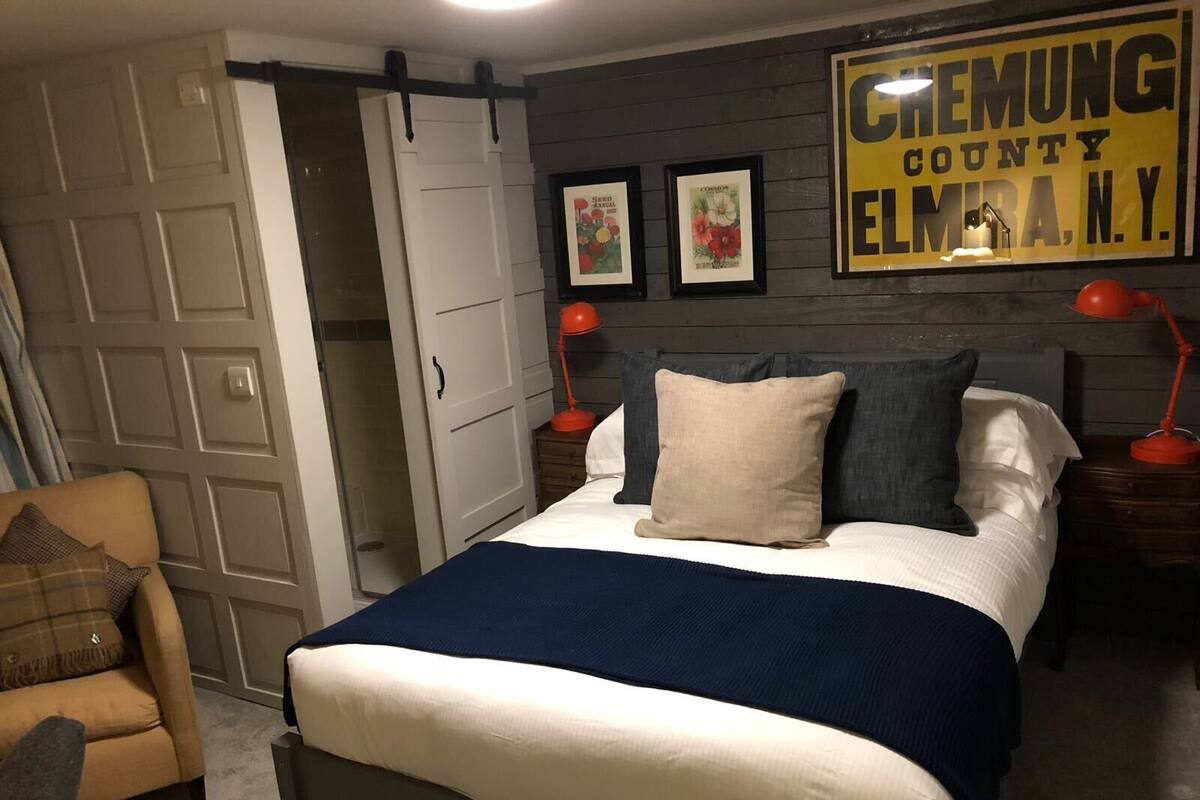 A bedroom with a bed, two nightstands, a chair, a wardrobe, and a wall with a framed sign.