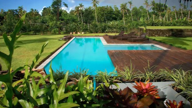 A swimming pool with a wooden deck, surrounded by lush greenery and palm trees. - Ifiele'ele Plantation (Fasito'o Uta)