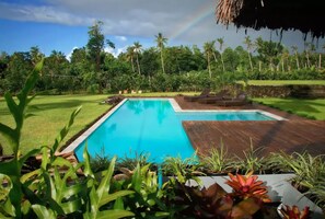 A swimming pool with a wooden deck, surrounded by lush greenery and palm trees. - Ifiele'ele Plantation (Fasito'o Uta)