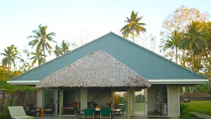 A house with a thatched roof patio, a covered outdoor seating area, and a stone wall. - Ifiele'ele Plantation (Fasito'o Uta)
