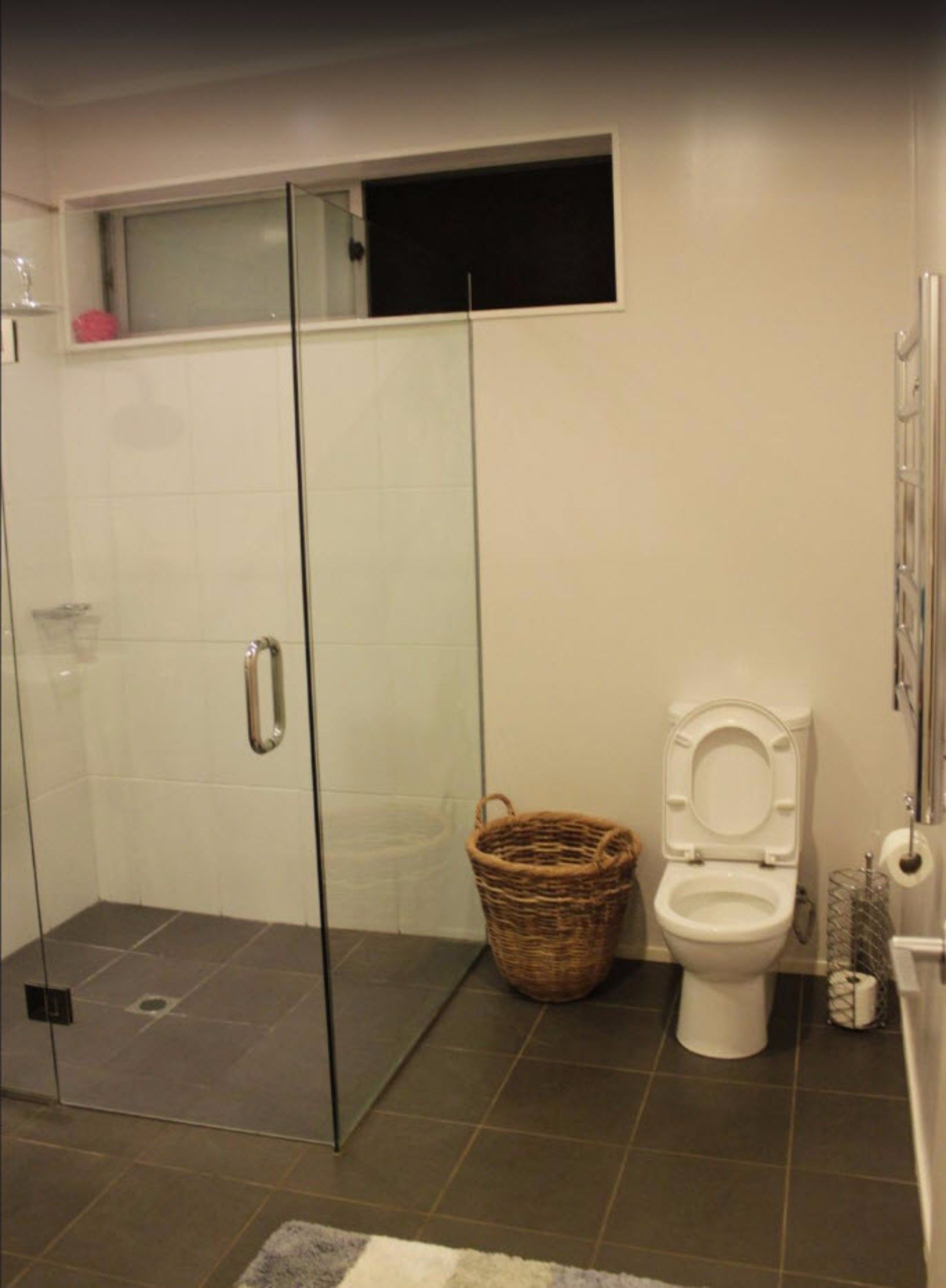 A bathroom with a glass shower enclosure, a white toilet, and a wicker basket.