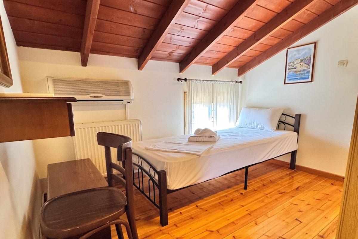 A cozy attic bedroom with a wooden floor, a bed, a chair, and a radiator.