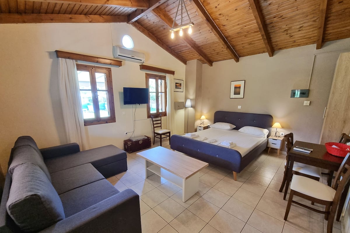 A cozy room with a bed, a sofa, a small table, a TV, and a window.