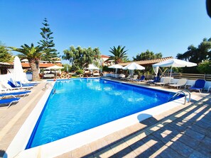 Une piscine entourée de palmiers et de bâtiments, avec des chaises longues et des parasols.