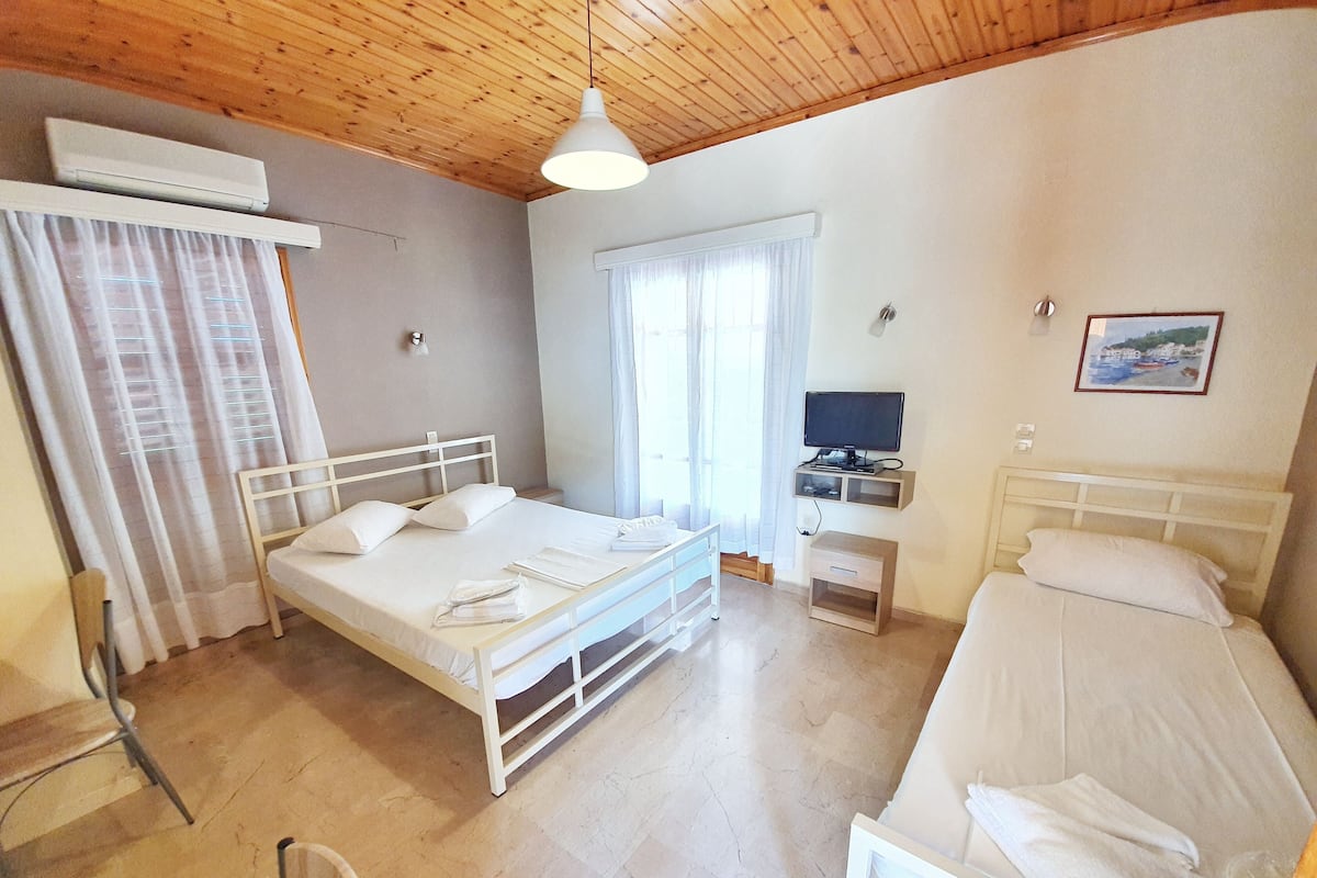 A bedroom with two beds, a desk, a TV, and an air conditioning unit.