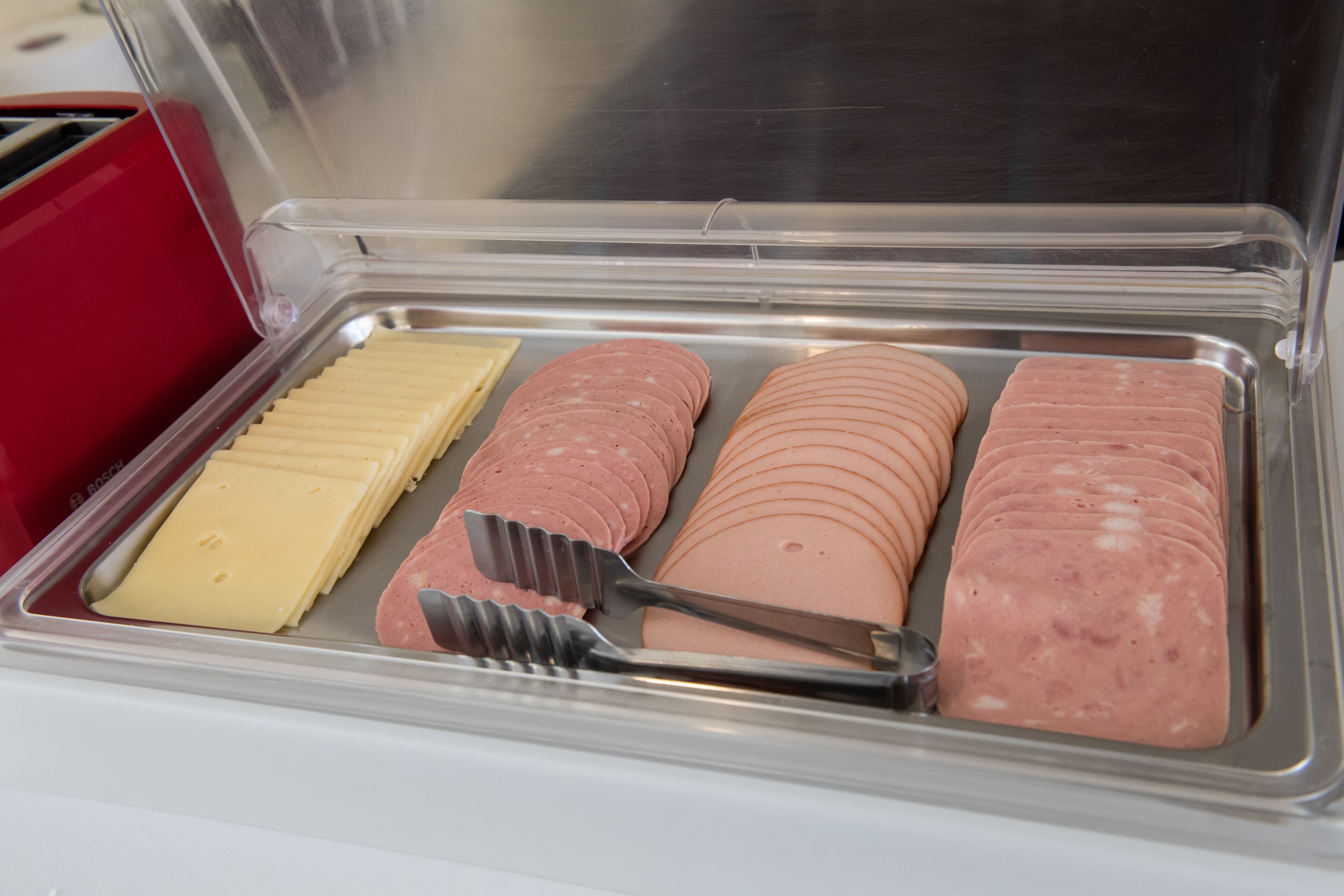 A food display with sliced meats and cheese in a clear container.