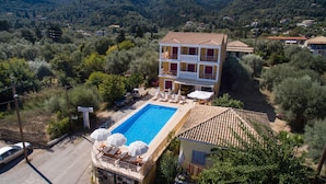 Un edificio de dos pisos con piscina, asientos al aire libre y vistas del paisaje circundante.