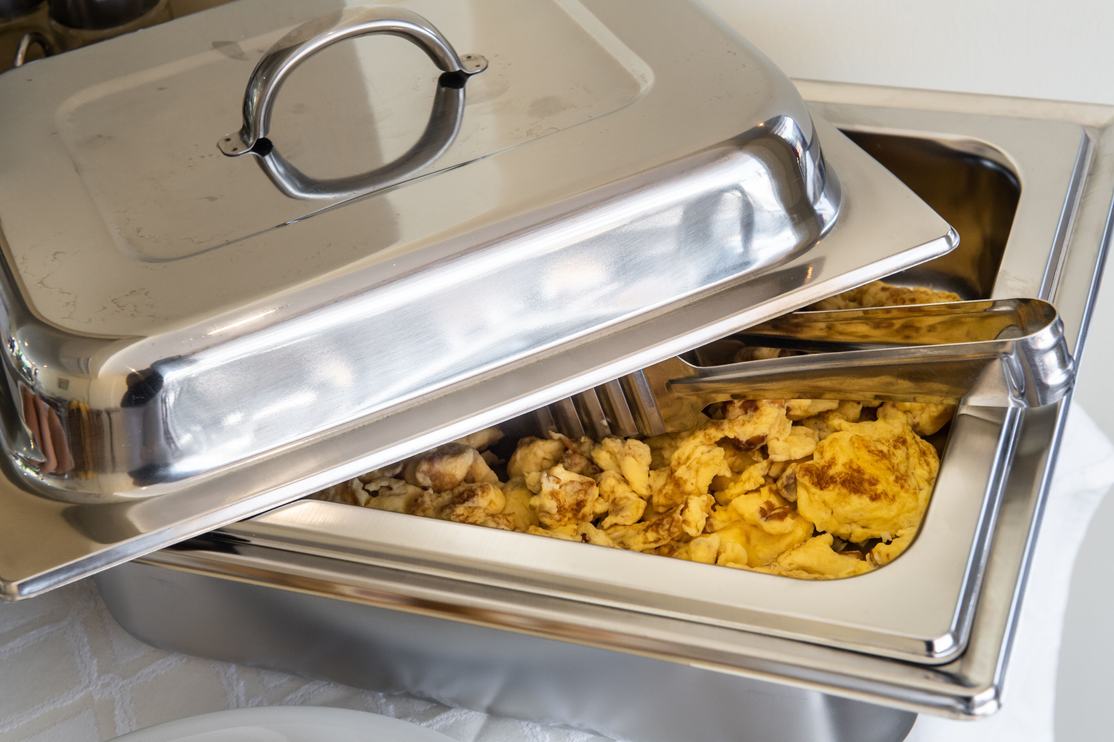 A buffet setup with a covered serving dish containing scrambled eggs and vegetables.