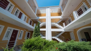 Un atrio de varios niveles con una escalera central, balcones y un cielo azul claro.