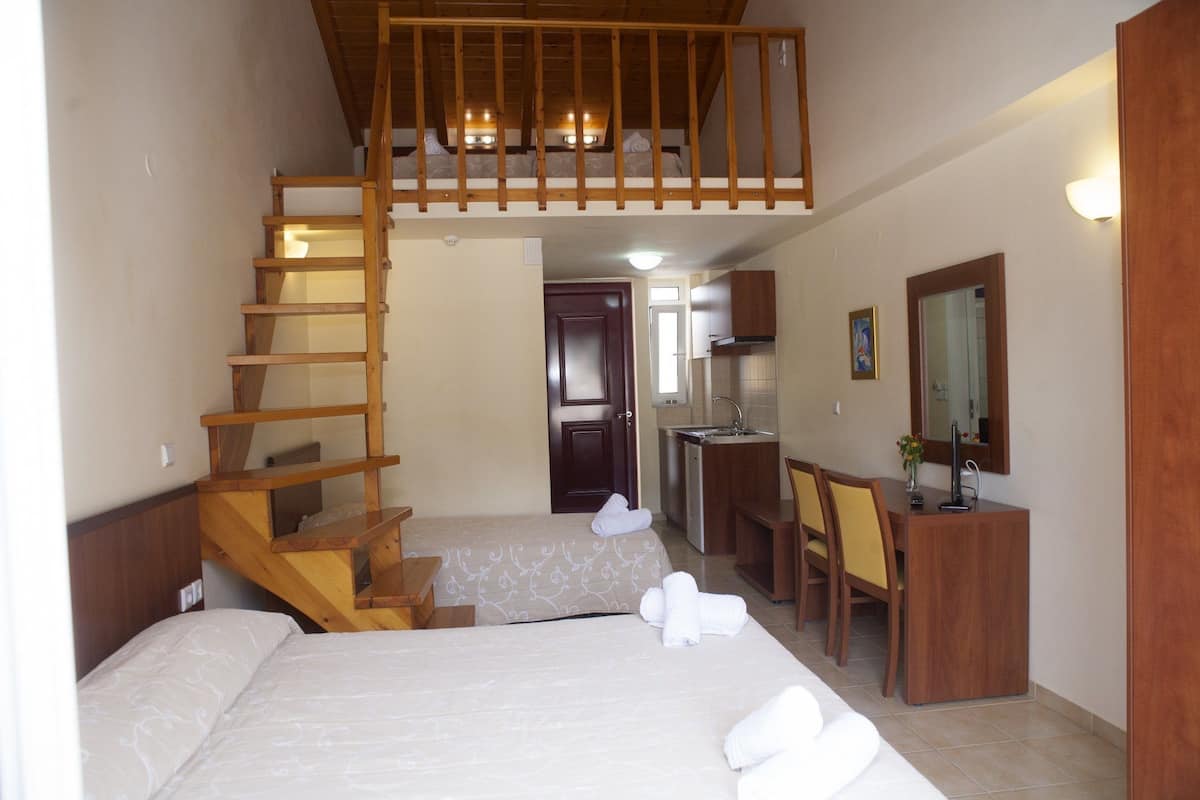 Ein Schlafzimmer mit einer Holztreppe, einem Bett, einem Schreibtisch mit Stuhl und einer Küchenzeile.