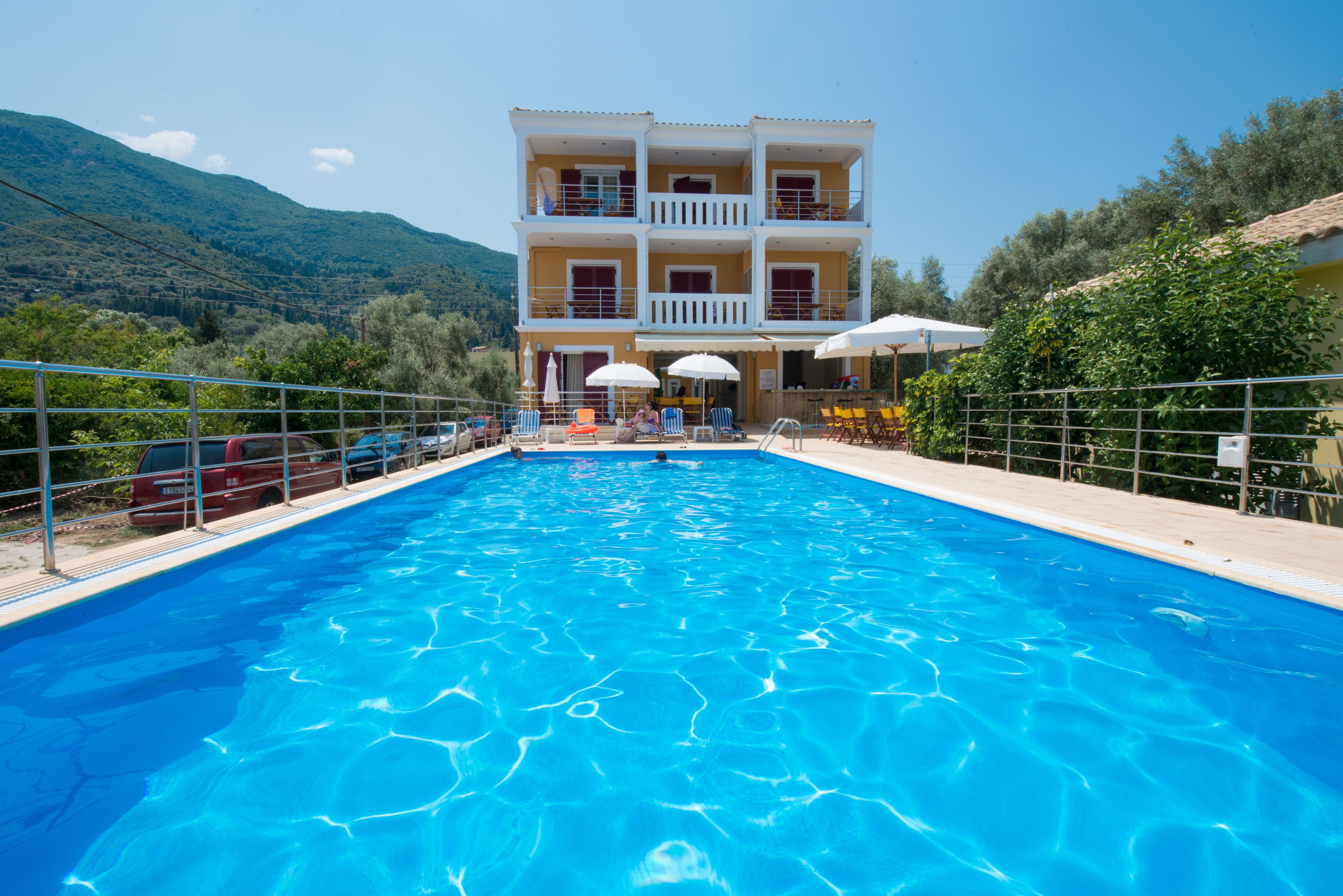 A swimming pool with a view of a two-story building, surrounded by greenery and a mountainous backdrop.