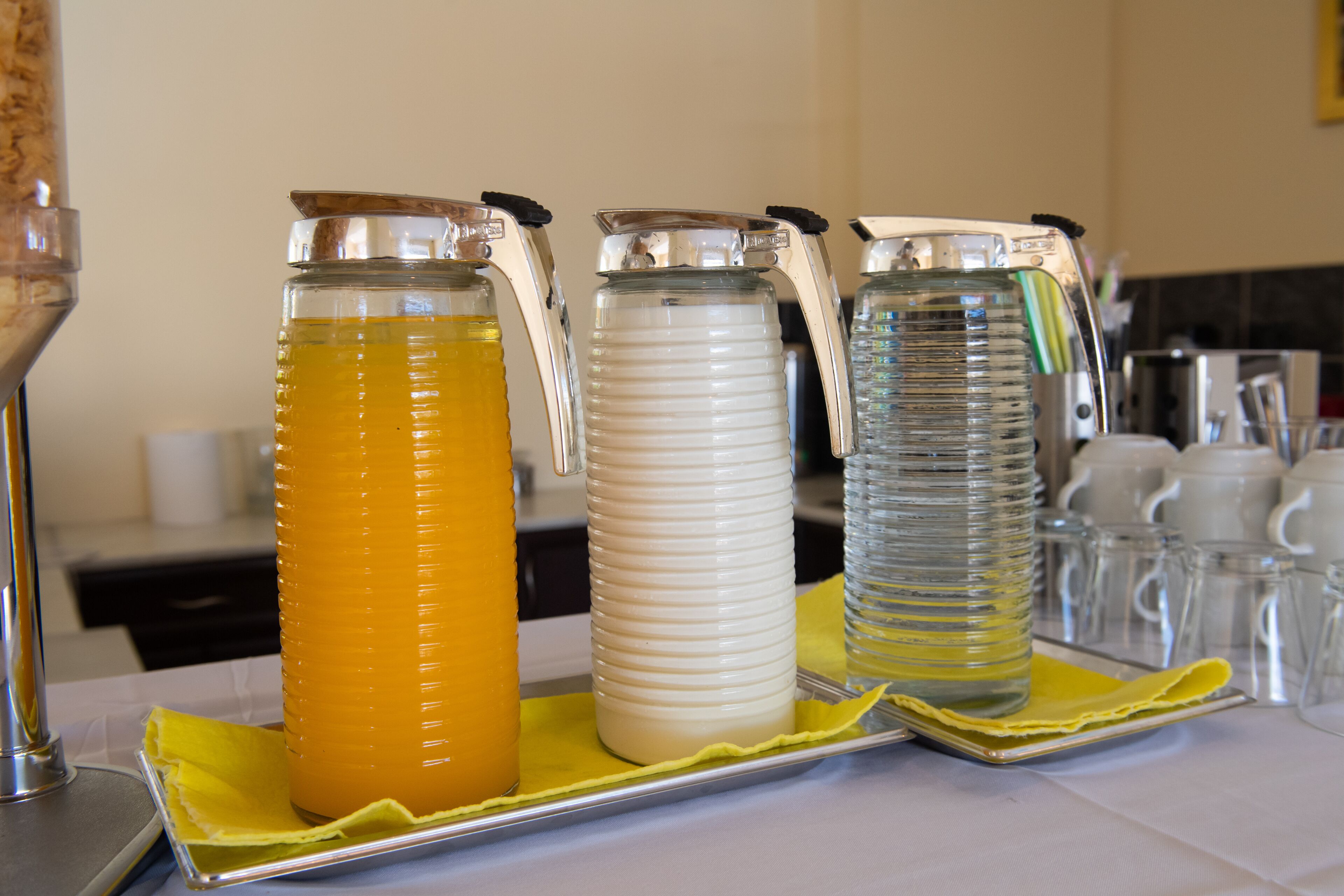 Three glass dispensers with handles on a tray.