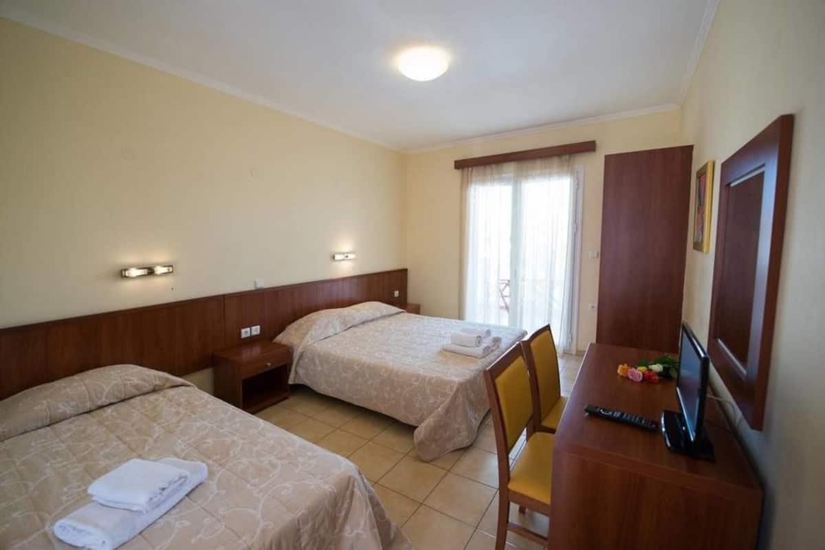 Ein Hotelzimmer mit zwei Betten, einem Schreibtisch mit Stuhl, einem Fernseher und einem Fenster mit Vorhängen.