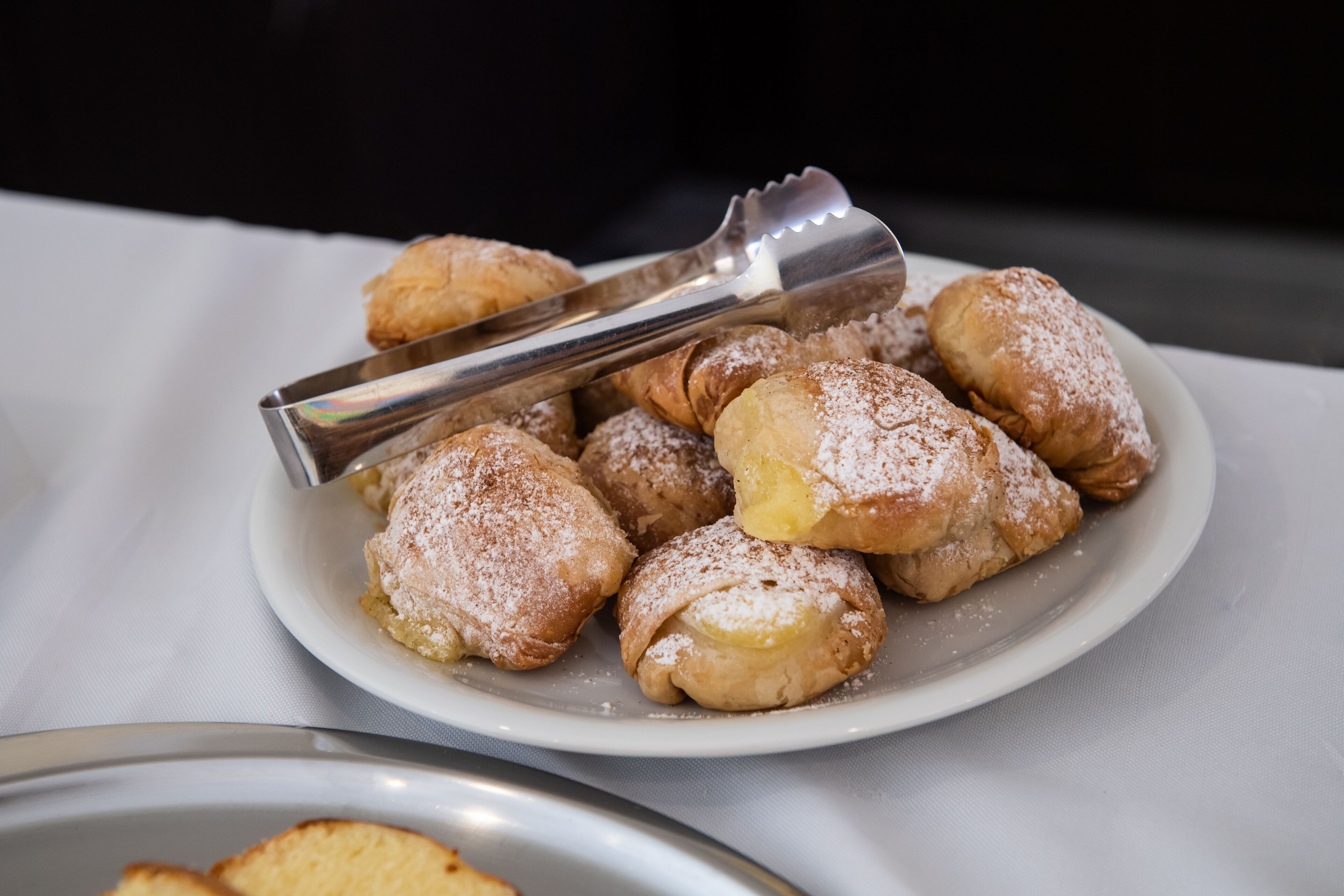 Een bord gebakjes bestrooid met poedersuiker, met een paar tangen er bovenop.
