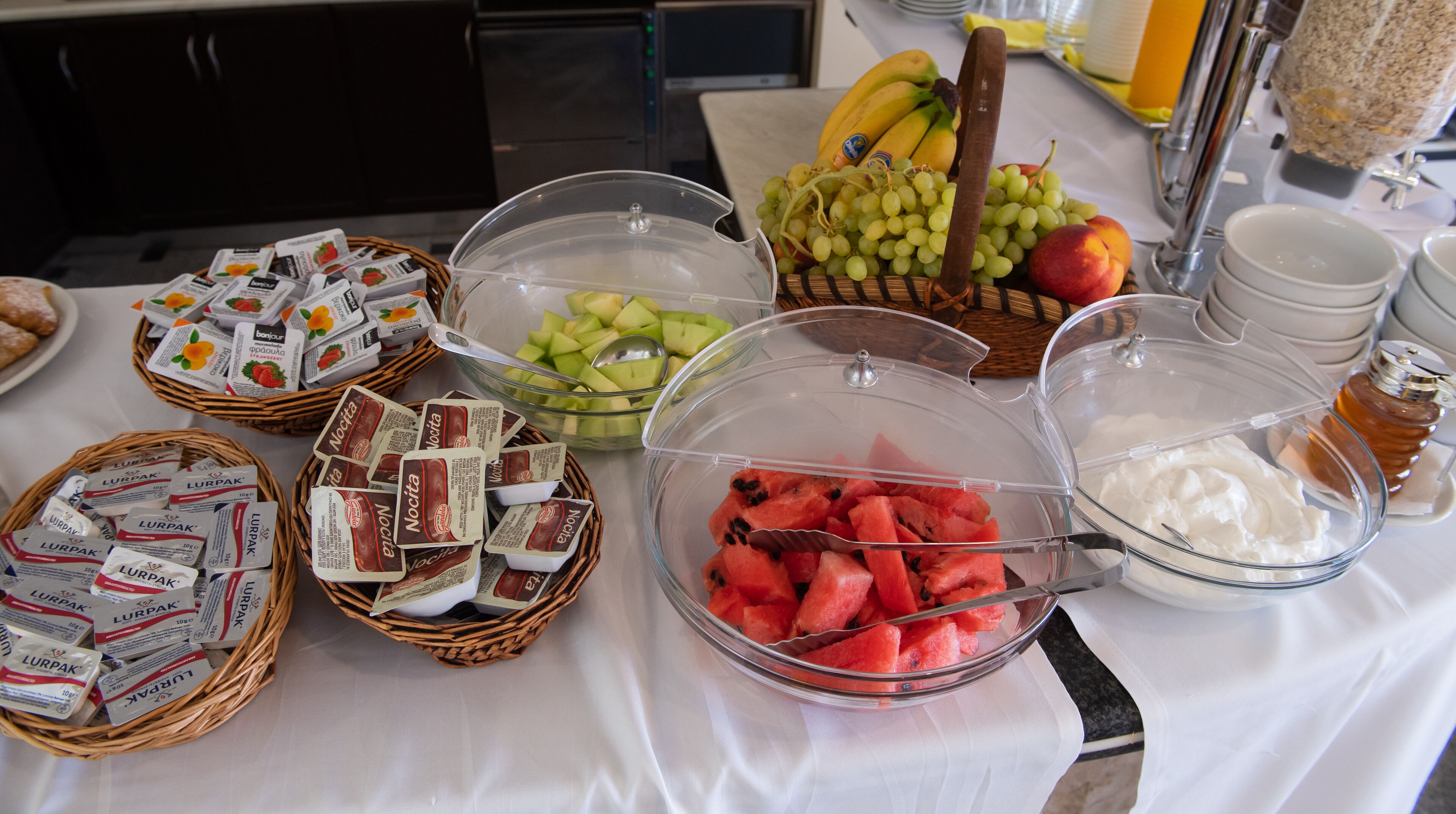 A buffet table with various food items including yogurt, watermelon, grapes, and honey.