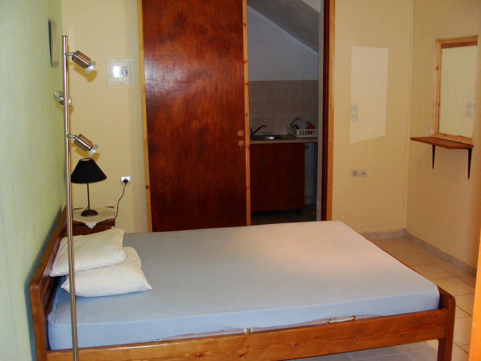 A bedroom with a wooden bed, a bedside lamp, a mirror, and a bathroom visible through an open door.