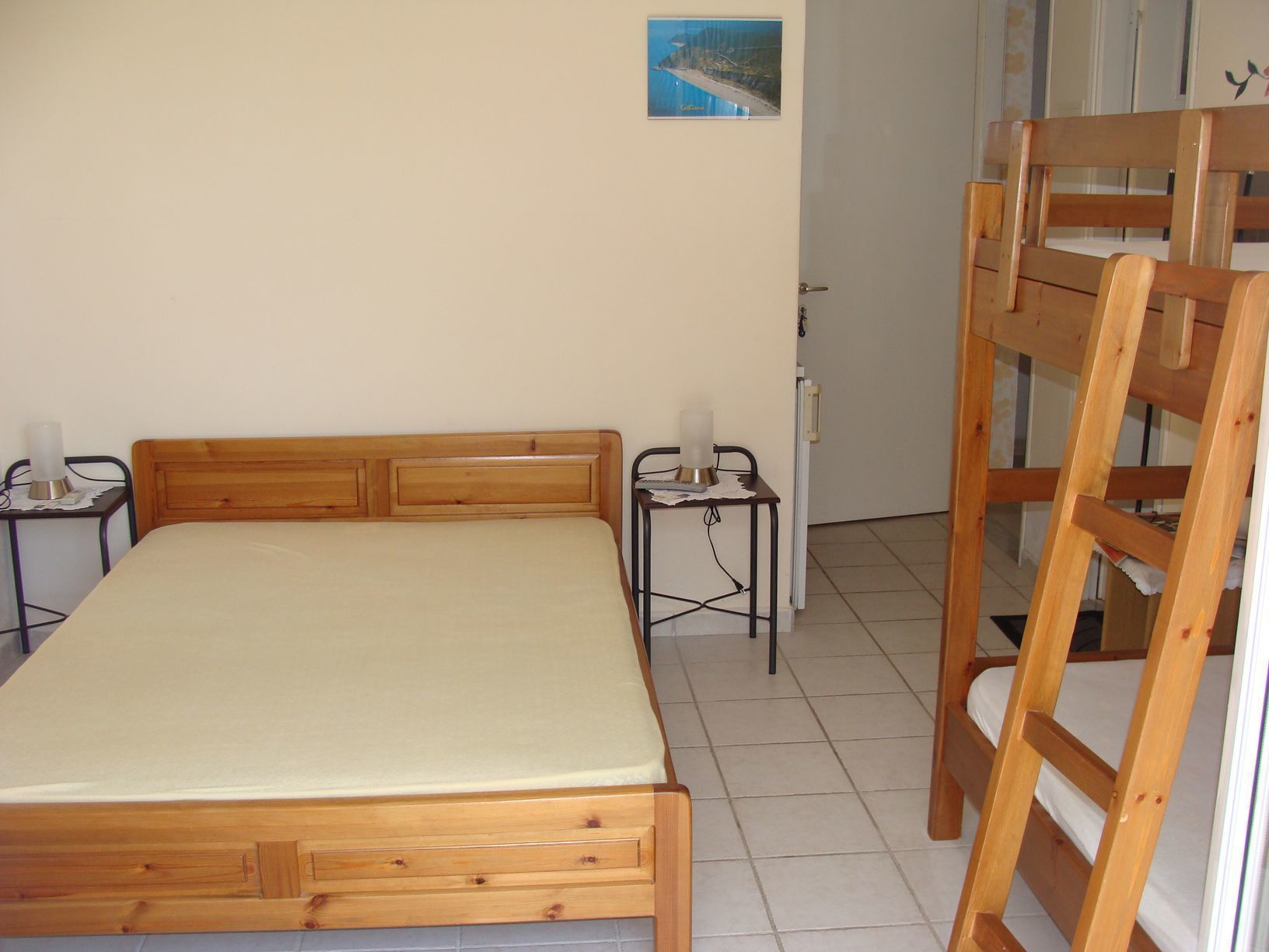 Una cama individual con cabecera de madera, una mesita de noche con lámpara y un cuadro pequeño en la pared.