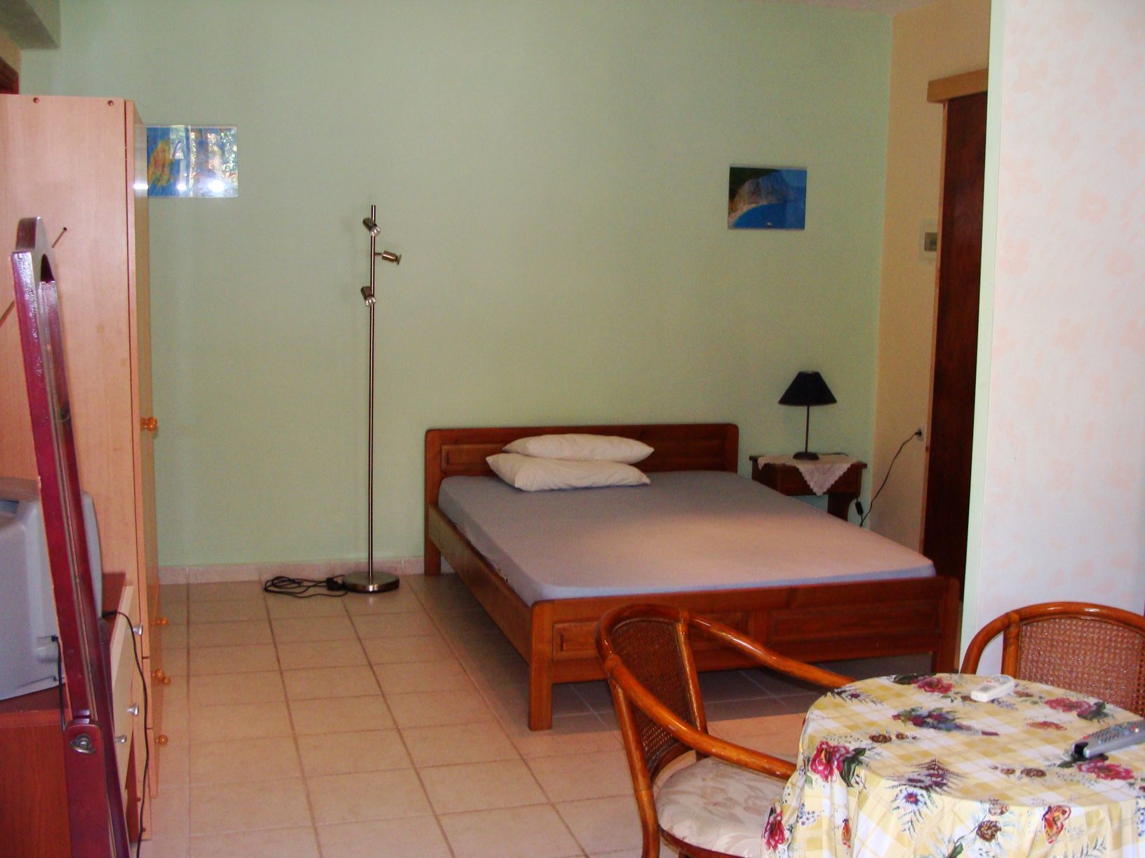 Un dormitorio con una cama individual, una mesita de noche con lámpara, una silla y una pequeña mesa con mantel floreado.