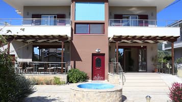 Un edificio de dos plantas con una puerta roja, una fuente de piedra y asientos al aire libre.