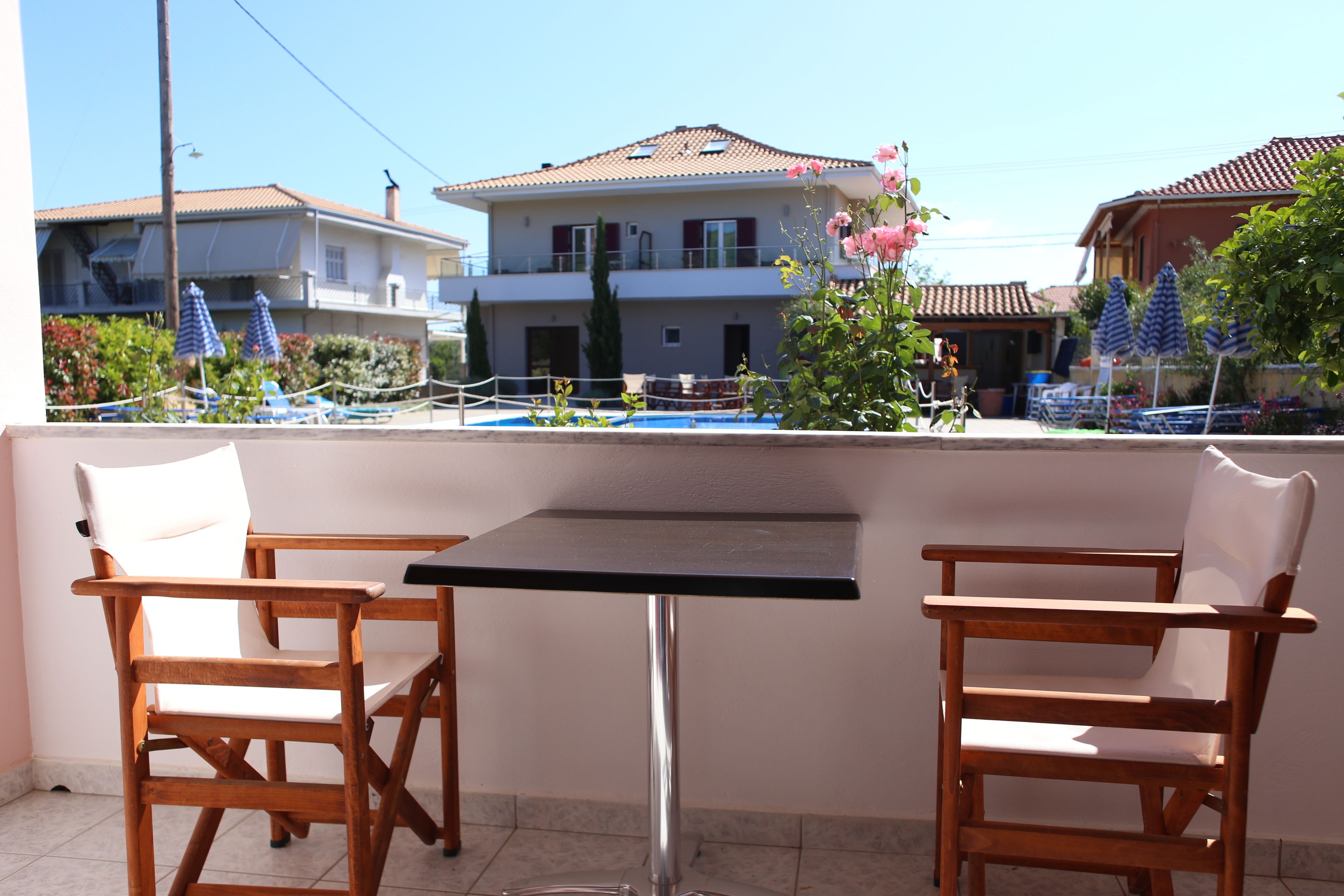 A balcony with two wooden chairs and a table, overlooking a residential area with houses and a swimming pool.