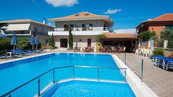 A swimming pool with lounge chairs and umbrellas, a building with a tiled roof, and a clear blue sky.