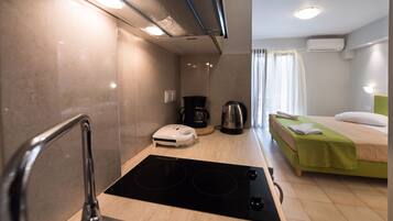 Una habitación de hotel compacta con kitchenette, una cama con ropa de cama verde, cafetera y un pequeño calentador.