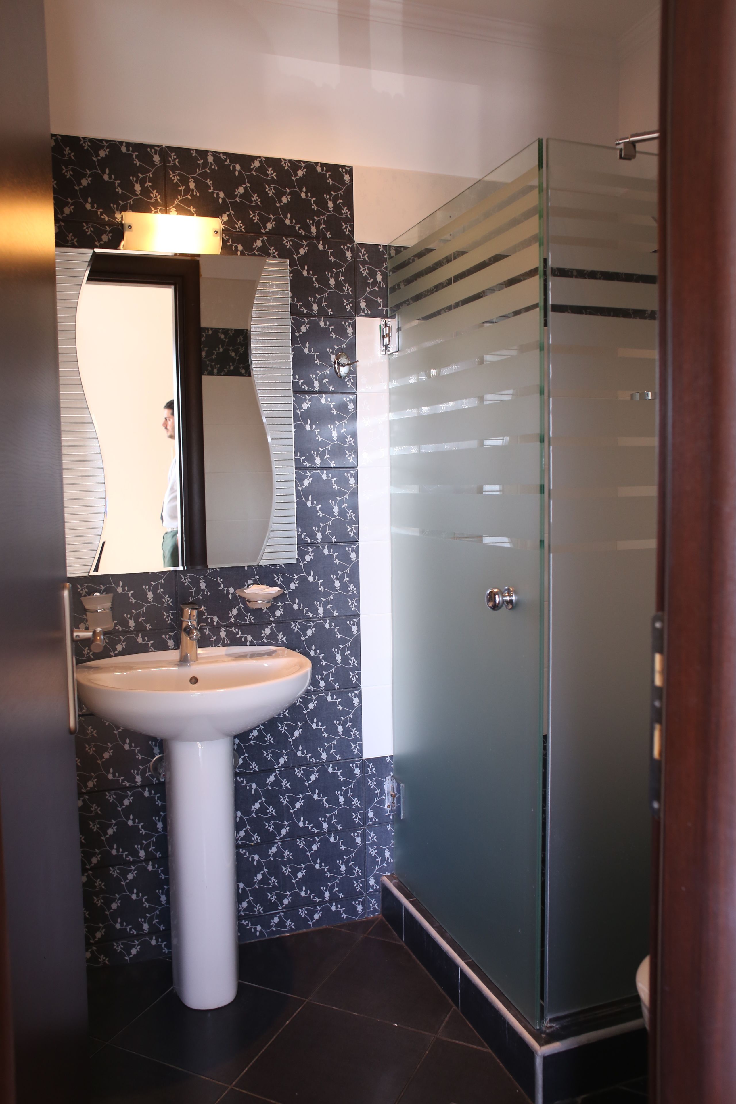 A bathroom with a white pedestal sink, a mirror, and a glass shower enclosure.
