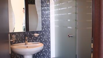 A bathroom with a white pedestal sink, a mirror, and a glass shower enclosure.