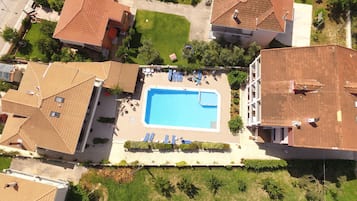 Vista aérea de una zona residencial con piscina rodeada de sillas de descanso y un muro de piedra.