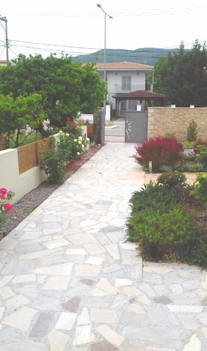 A stone pathway leading to a house with a tiled roof, surrounded by various plants and shrubs. - Christina Studios (Lefkada)