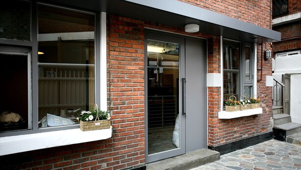 Un edificio de ladrillo con puerta de cristal, escalones de piedra y macetas de flores en los alféizares de las ventanas.