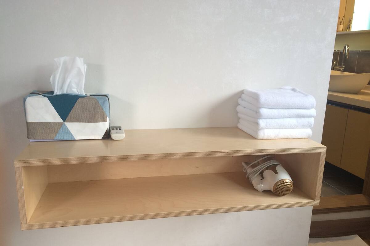 A wooden shelf with a tissue box, a remote control, and folded towels.