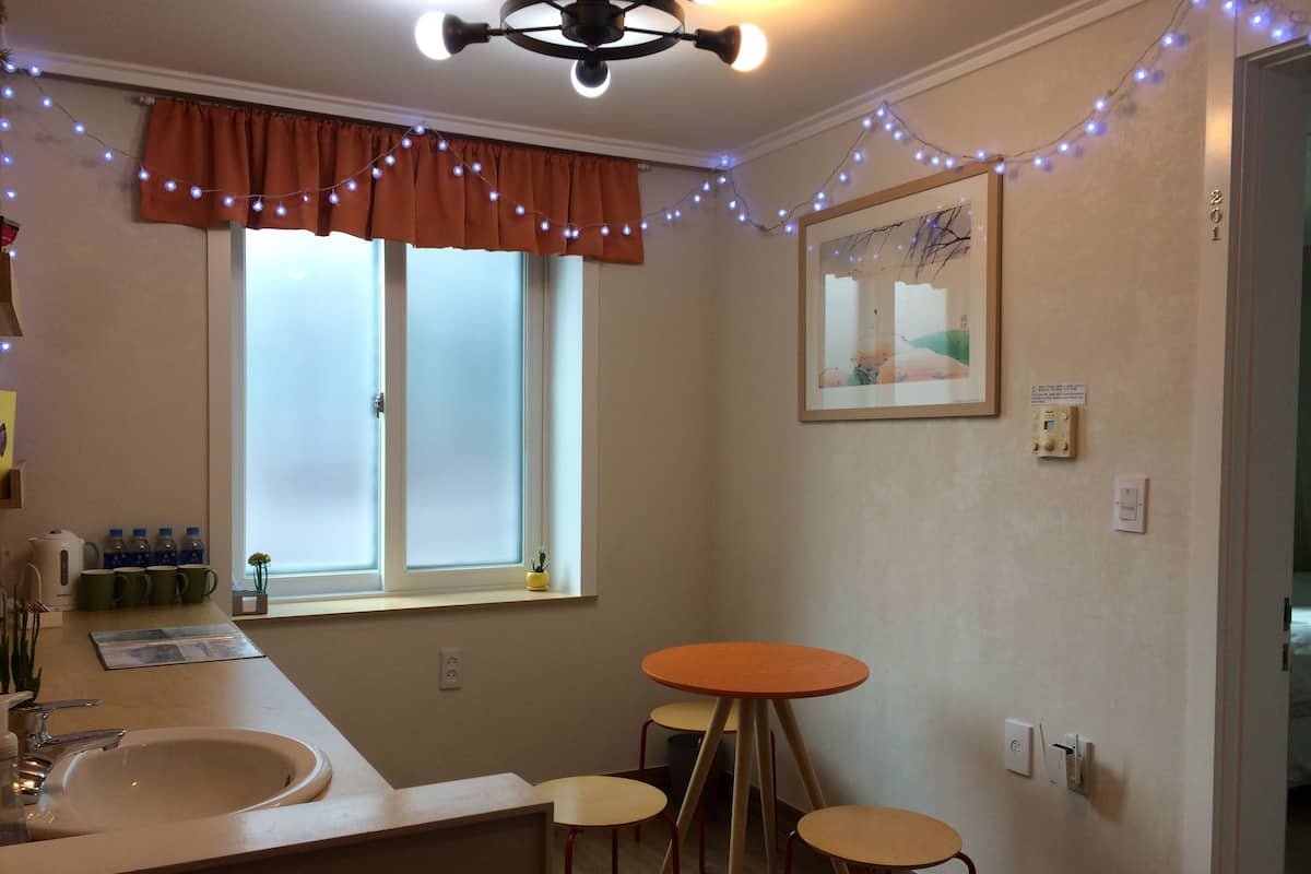 A small kitchenette with a sink, a window with frosted glass, a ceiling fan, and a small table with two stools.
