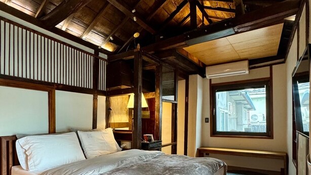 A bedroom with a large bed, wooden beams, a window with a view, and a small table with a lamp. - Nook Seoul (Seoul)