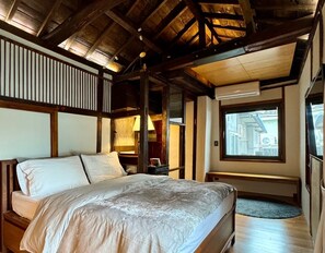 A bedroom with a large bed, wooden beams, a window with a view, and a small table with a lamp. - Nook Seoul (Seoul)