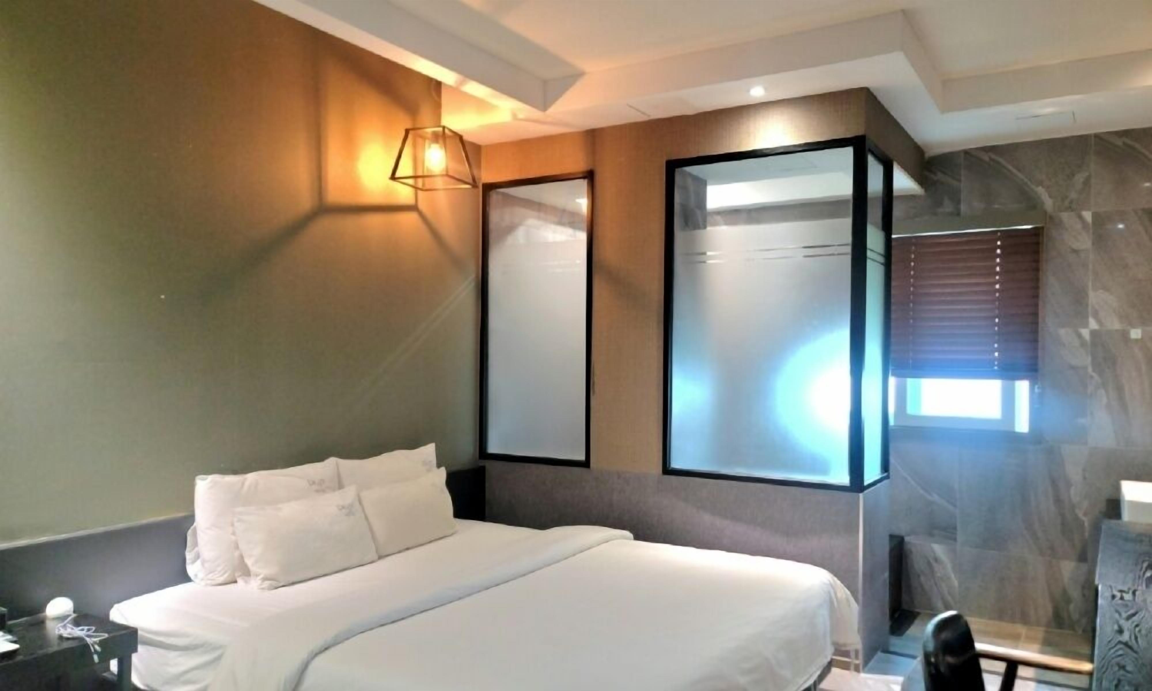 Una habitación de hotel moderna con una cama grande, una mesita de noche, un espejo y una lámpara fijada a la pared.