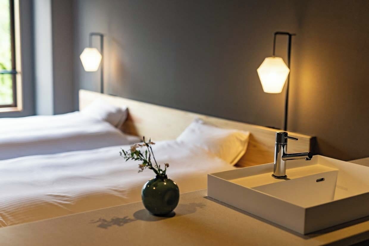 Quarto de hotel com uma cama, uma mesa de cabeceira com um vaso e uma pia moderna.