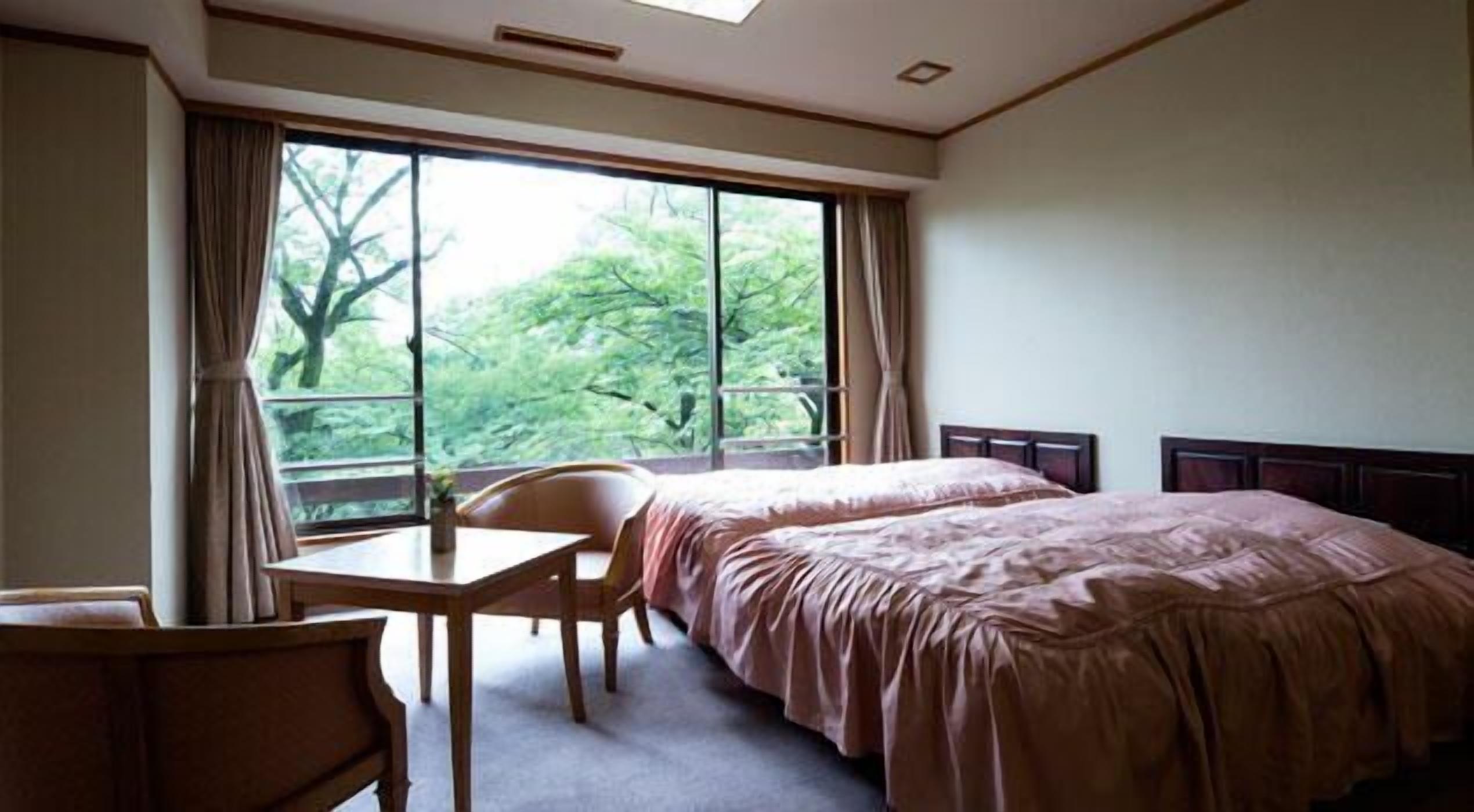 Habitación de hotel con una cama grande, un escritorio pequeño, una silla y una ventana que da a vistas de árboles.
