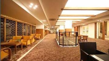 A hotel lobby with a patterned carpet, seating area with yellow chairs, a glass partition, and a wall with a patterned design.