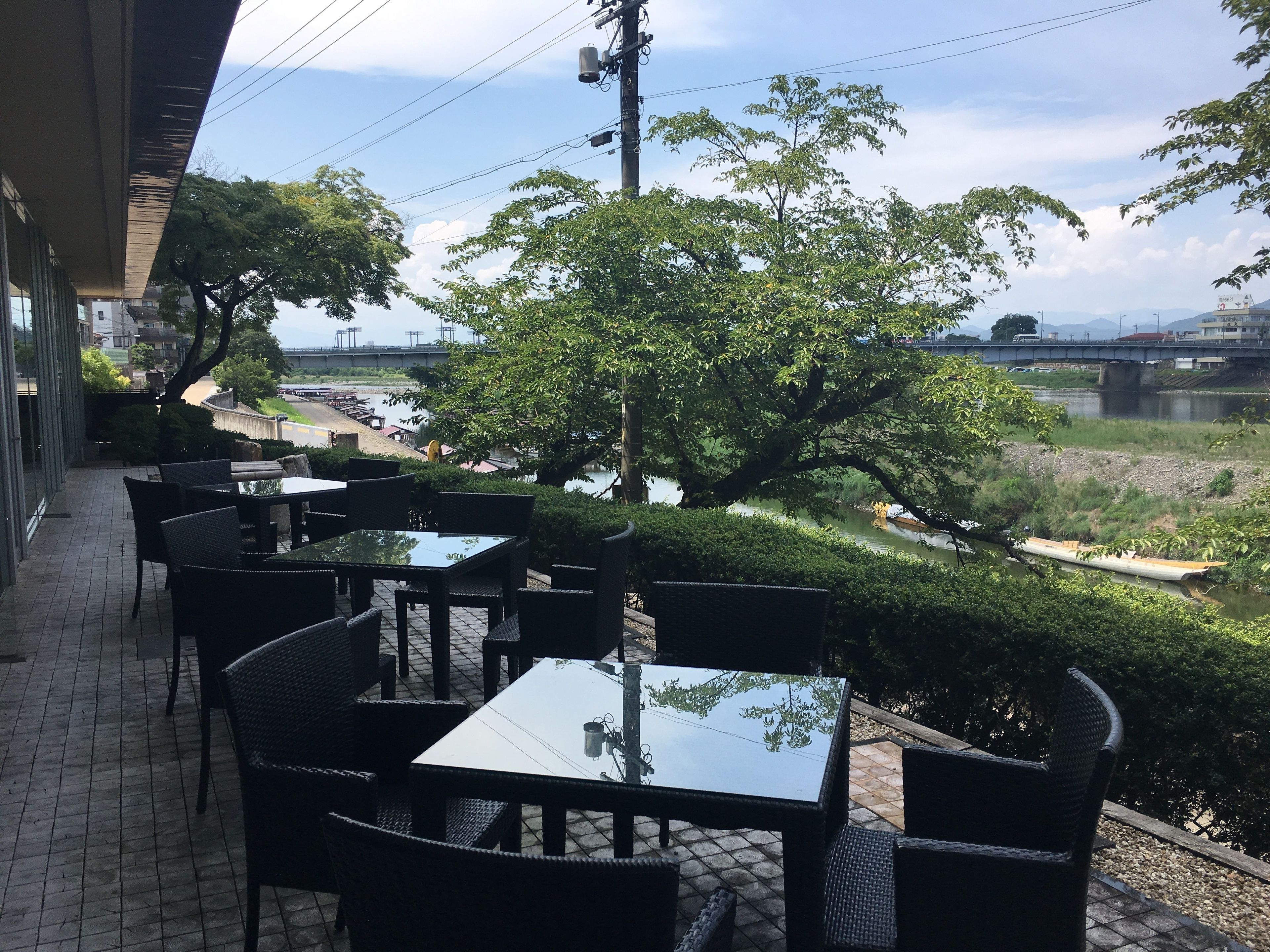 An outdoor patio with tables and chairs overlooking a river and a bridge.