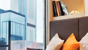 A modern room with a city view, a sofa with cushions, a tray with pastries, and a bookshelf with books. - Burlington Hotel (Hong Kong)